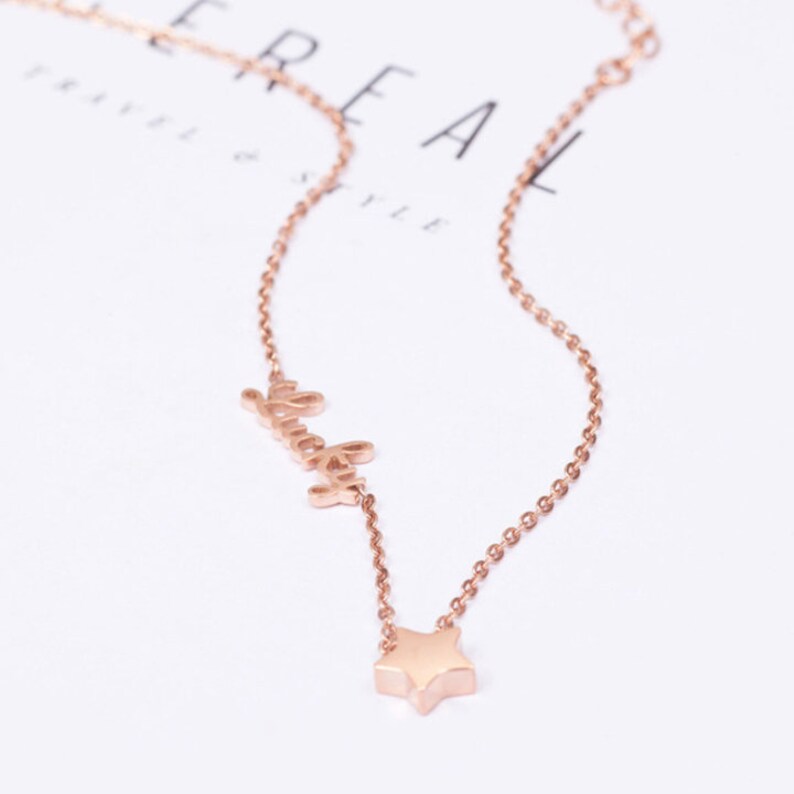 Puede incluir: Un collar de oro rosa con un dije de estrella y la palabra "lucky".
