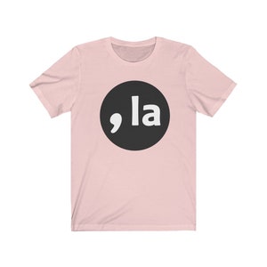 May include: A pink t-shirt with a black circle and white text that says ",la"