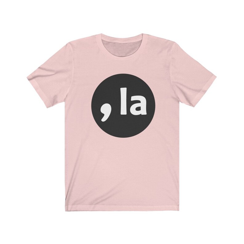 May include: A pink t-shirt with a black circle and white text that says ",la"