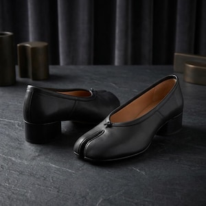 Peut inclure: Une paire de chaussures à talons en cuir noir avec un design à bout fendu. Les chaussures ont un petit talon bloc et un petit nœud sur le dessus. La doublure intérieure est de couleur beige clair.