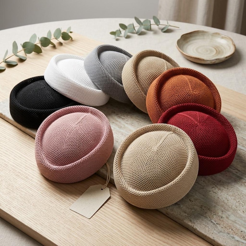 May include: A collection of nine round, brimless hats in various solid colors including black, white, gray, beige, orange, red, pink, and tan. Each hat features a dense, uniform knit texture and a rolled edge. A blank rectangular tag hangs from one hat.