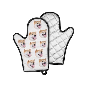 Könnte beinhalten: Ein weißer Topflappen mit schwarzem Rand und einem Muster aus Shiba Inu-Hundegesichtern. Die Rückseite des Topflappens ist silberfarben und gesteppt.