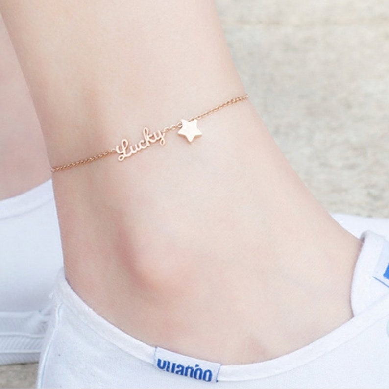 Puede incluir: Un tobillo de cadena dorada con un dije de estrella y la palabra "Lucky" escrita en cursiva.