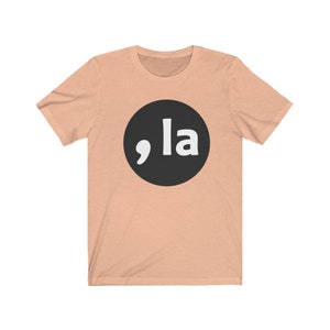 May include: A peach-colored t-shirt with a black circle containing a white comma and the word "la" in white.