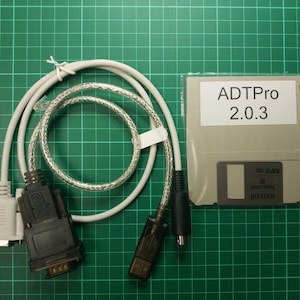 Könnte beinhalten: Ein weißes Kabel mit zwei Steckern, einem grauen und einem schwarzen, und einer Diskette mit der Aufschrift "ADTPro 2.0.3".