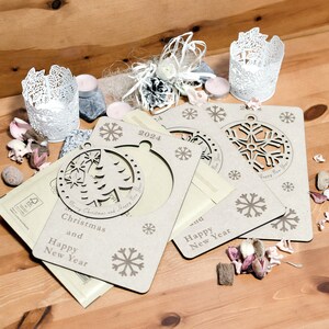 May include: Three wooden Christmas ornaments with a snowflake design and the text "Merry Christmas and Happy New Year" and "Happy New Year". The ornaments are on a wooden surface with decorative items.
