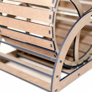 May include: A light brown wooden organizer featuring a slatted, curved design with dark edges. The structure is composed of interlocking panels forming a cylindrical shape with horizontal slats, showcasing a layered, geometric construction.