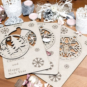 May include: Three wooden Christmas ornaments with cut-out designs of a Christmas tree, snowflake, and a snowflake. The ornaments are brown and have the text "Merry Christmas and Happy New Year" and "2024" printed on them.