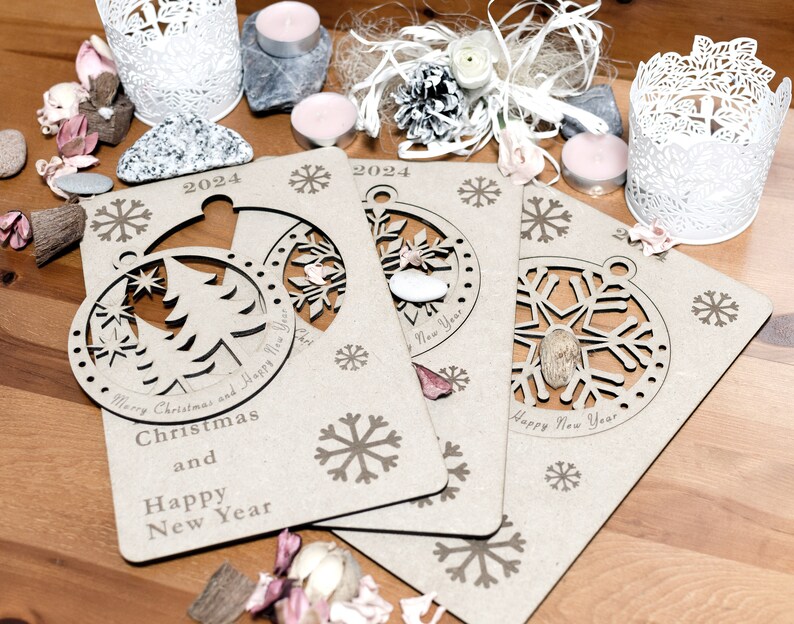 May include: Three wooden Christmas ornaments with cut-out designs of a Christmas tree, snowflake, and a snowflake. The ornaments are brown and have the text "Merry Christmas and Happy New Year" and "2024" printed on them.