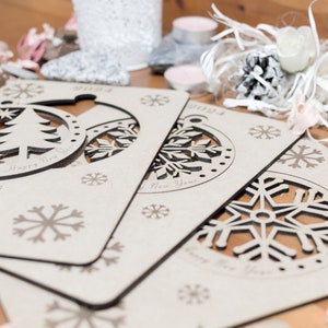 May include: Three wooden Christmas ornaments with cut-out designs. The ornaments are in the shape of a Christmas tree, a snowflake, and a snowflake. The ornaments are decorated with the words "Merry Christmas and Happy New Year" and "Happy New Year".