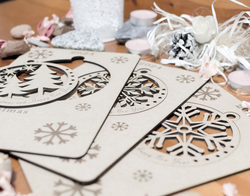 May include: Three wooden Christmas ornaments with cut-out designs. The ornaments are in the shape of a Christmas tree, a snowflake, and a snowflake. The ornaments are decorated with the words "Merry Christmas and Happy New Year" and "Happy New Year".
