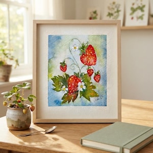 Può includere: Un dipinto ad acquerello incorniciato raffigurante fragole rosse, foglie verdi e piccoli fiori bianchi su uno sfondo sfumato blu e verde. L'opera è racchiusa in una cornice di legno chiaro con carta dai bordi irregolari.