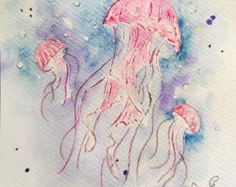 Könnte beinhalten: Aquarellmalerei von drei rosa Quallen mit langen, fließenden Tentakeln. Die Quallen sind vor einem blau-violetten Aquarellhintergrund mit kleinen weißen und violetten Punkten platziert. Das Kunstwerk ist unten rechts signiert.
