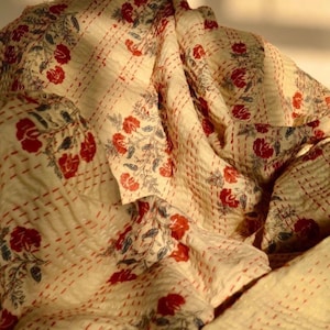May include: A cream-colored kantha quilt with a red and blue floral pattern. The quilt is made of cotton and has a hand-stitched design.