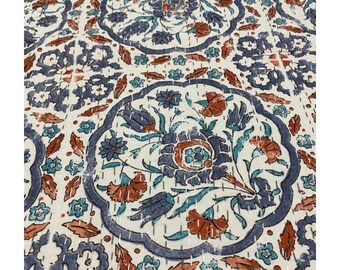 May include: Cream-colored textile with a repeating floral pattern in shades of blue, teal, and rust. The design features stylized flowers and leaves within a dark blue scalloped border, stitched with white thread. The overall aesthetic is reminiscent of traditional block printing.