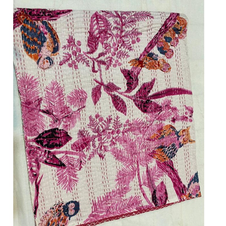 Puede incluir: Una colcha kantha rosa y blanca con un dise&ntilde;o floral y de p&aacute;jaros. La colcha est&aacute; hecha de algod&oacute;n y est&aacute; cosida a mano.