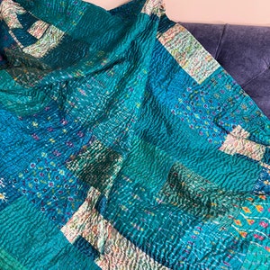 May include: A teal blue kantha quilt made from recycled saris. The quilt is patchwork with different patterns and textures. It is a traditional Indian textile.