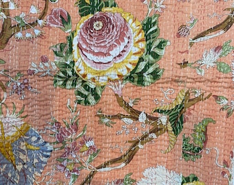 May include: A peach-colored fabric with a floral pattern. The flowers are pink, white, and yellow with green leaves. The fabric has a quilted texture.