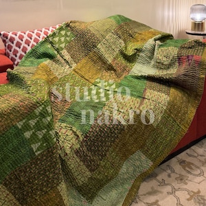 May include: A patchwork quilt in shades of green, brown, and yellow, draped over a red sofa. The quilt features a variety of stitched patterns and textures. The text "studio nakro" is visible on the quilt.
