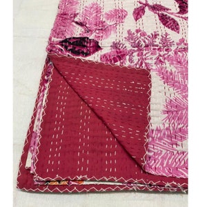 Puede incluir: Una colcha kantha floral rosa y blanca con un reverso rojo. La colcha est&aacute; doblada por la mitad y las costuras son visibles.