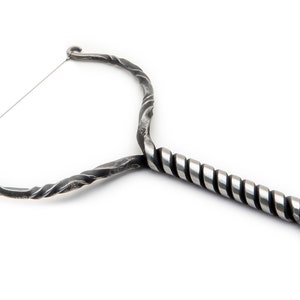 May include: A silver metal cheese cutter with a twisted handle and a wire loop. The handle is twisted and has a loop at the end.