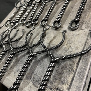 May include: A collection of metal bottle openers with a twisted design. The openers are hanging on a wire rack and have a loop at the top for hanging.