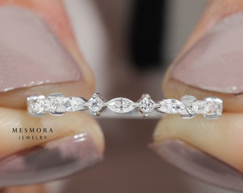 May include: A silver-toned band ring featuring a repeating pattern of marquise-cut and round-cut clear stones set in a delicate metal frame. The ring displays a symmetrical arrangement of alternating stone shapes across the entire visible band.