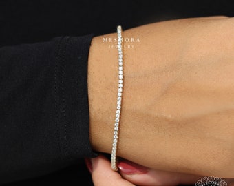 Könnte beinhalten: Ein goldenes Tennisarmband mit einer Reihe kleiner, klarer Diamanten. Das Armband wird am Handgelenk getragen.