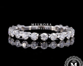 May include: A silver-toned eternity band featuring a continuous row of round, clear, faceted stones set in metal. The text MESMORA JEWELRY is centered above the ring, and a circular logo with the letter M is in the bottom right corner.
