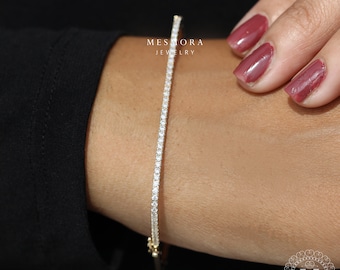 Könnte beinhalten: Ein zartes Tennisarmband aus Gold mit einer Reihe funkelnder Diamanten. Das Armband wird am Handgelenk einer Person gezeigt.