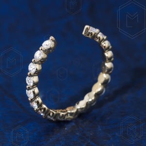 May include: A gold ring with a row of small, clear diamonds set in a curved band.