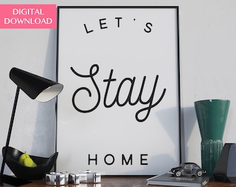 Może przedstawiać: Czarno-biała drukowalna grafika ścienna z tekstem "Let's Stay Home". Grafika jest oprawiona w czarną ramę i umieszczona na drewnianej półce z lampą, wazą i małym samochodem.
