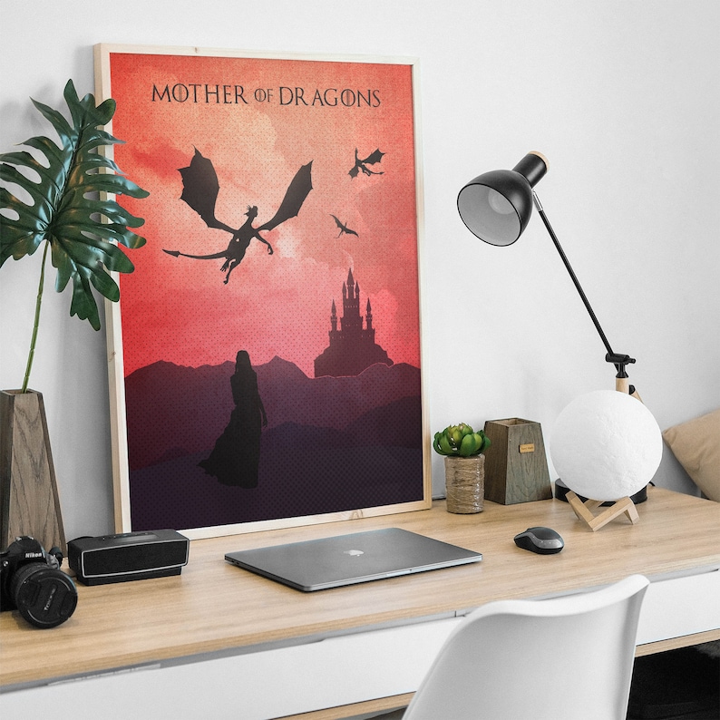 May include: A framed print with a red and orange gradient background. The print features a silhouette of a dragon flying over a castle with the text "Mother of Dragons" at the top.