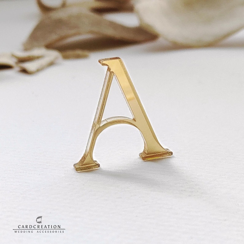 May include: A gold-coloured letter "A" in a serif font, possibly for wedding decorations or crafts. The letter is made of a shiny material and rests on a white surface. The logo "CARDCREATION WEDDING ACCESSORIES" is visible at the bottom.
