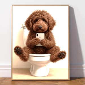Może przedstawiać: Oprawiony wydruk przedstawiający brązowego psa Goldendoodle siedzącego na białej toalecie, trzymającego biały smartfon. Pies ma puszyste futro i jest w centrum uwagi. Tło to gładka biała ściana.
