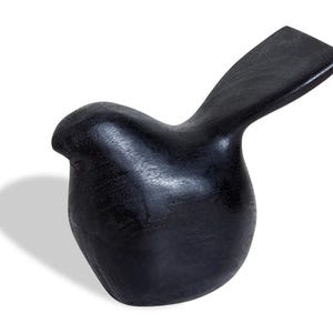 May include: A solid, black wooden bird sculpture with a smooth, polished finish. The bird has a rounded body and a raised tail, creating a simple yet elegant design. The sculpture is likely a decorative item.