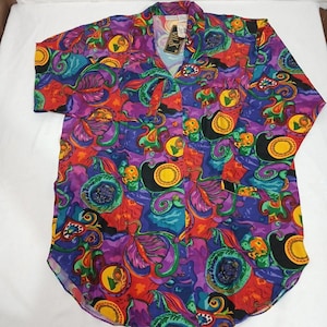 May include: A colorful button-down shirt with a vibrant pattern of purple, red, blue, and yellow abstract shapes. The shirt has short sleeves and a V-neck collar. A tag that says "Silk" is attached to the shirt.