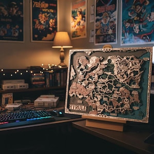 May include: A detailed wooden map of Hyrule, featuring a layered design with brown and green tones. The map is displayed on a wooden stand, with the word "HYRULE" at the bottom. The map is on a desk with a keyboard and mouse.