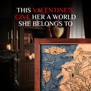 May include: A framed wooden map with a dark brown frame. The map features a detailed design with a blue ocean and landmasses in shades of brown. The text "THIS VALENTINE'S, GIVE HER A WORLD SHE BELONGS TO" is at the top.