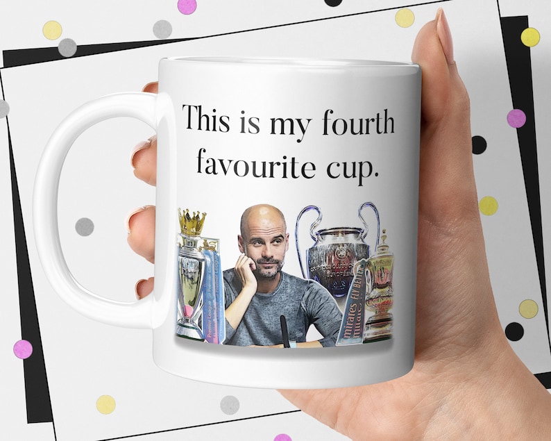 K&ouml;nnte beinhalten: Wei&szlig;e Keramik-Tasse mit dem Text "This is my fourth favourite cup." und einem Bild eines Mannes und Troph&auml;en. Die Tasse hat einen gebogenen Henkel und wird von einer Person gehalten.