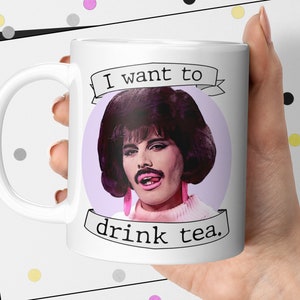May include: White ceramic mug with a purple background and a cartoon image of Freddie Mercury with the text "I want to drink tea."