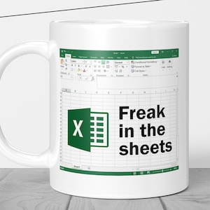 May include: White coffee mug featuring a green Microsoft Excel logo and the text "Freak in the sheets" on a white background.