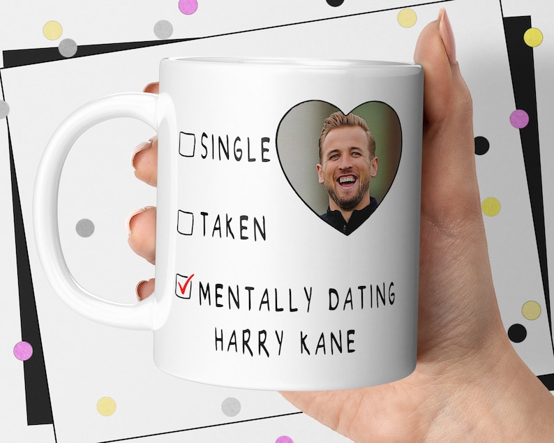 Pu&ograve; includere: Tazza in ceramica bianca con la scritta "Single", "Taken" e "Mentally Dating Harry Kane". Una foto di Harry Kane &egrave; all'interno di una forma a cuore. La tazza &egrave; tenuta da una persona.