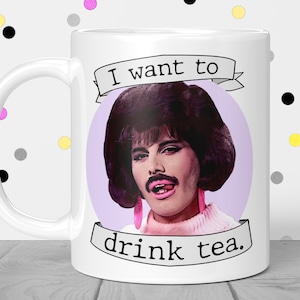 May include: White ceramic mug with a purple background and a picture of Freddie Mercury with the text "I want to drink tea."