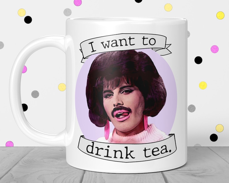 May include: White ceramic mug with a purple background and a picture of Freddie Mercury with the text "I want to drink tea."