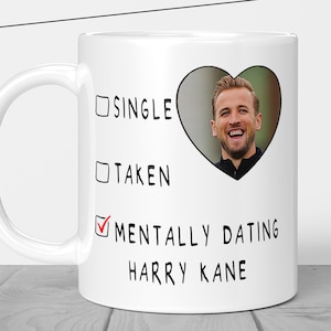 Pu&ograve; includere: Tazza in ceramica bianca con manico nero. La tazza presenta il testo "SINGLE", "TAKEN" e "MENTALLY DATING HARRY KANE" con un segno di spunta accanto all'ultima opzione. Sulla tazza &egrave; presente anche una foto a forma di cuore di un uomo sorridente.