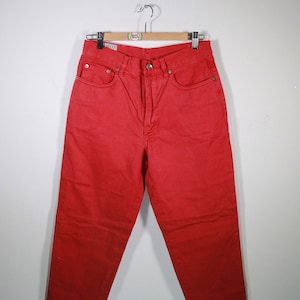 May include: Red denim jeans with a straight leg fit. The jeans have a classic five-pocket design and a button fly.
