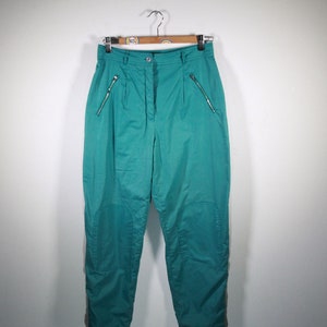 May include: Teal ski pants with side zipper pockets and white piping down the sides.