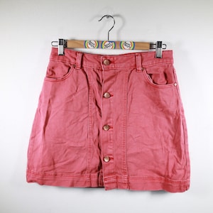 May include: A coral pink denim mini skirt with a button front closure. The skirt has a classic A-line silhouette and is made of a soft, comfortable fabric.