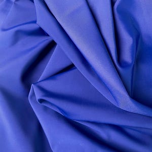 Può includere: Un primo piano di un tessuto liscio di colore blu reale. Il tessuto è piegato e drappeggiato, mostrando la sua morbida consistenza.
